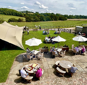 Image shows visitors relaxing in the sun at Denstone Hall Cafe and Farm Shop, near Uttoxeter, Staffordshire